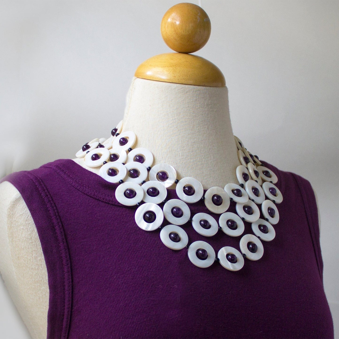Amethyst shell necklace with three layers of round disc shells and beads on mannequin with purple shirt